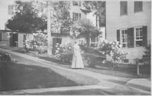 SA0288 - "In the Path:" shows a woman carrying a basket; buildings are behind her. Identified on the back along with an advertisement for other views. Associated with the North Family.